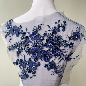 May include: Navy blue floral applique with beaded accents on a sheer mesh fabric. This applique is perfect for adding a touch of elegance to any garment.