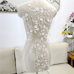 May include: White floral applique with beaded details on a sheer fabric background. The applique features delicate flowers and leaves, perfect for adding a touch of elegance to a garment.