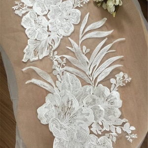 May include: White floral lace applique featuring delicate leaves and flowers. This lace applique is ideal for adding a touch of elegance to any project.