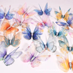 May include: A collection of decorative butterfly ornaments featuring translucent, layered wings in various pastel and vibrant gradients of blue, orange, pink, and purple. Each butterfly has a central body with a shimmering, jewel-like accent.