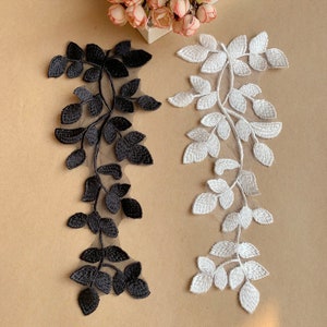 May include: Two pieces of black and white embroidered lace trim with a leaf design. The lace is on a beige background.