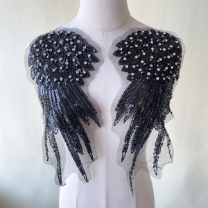 Può includere: Un paio di ali d'angelo nere di paillettes con decorazioni di cristallo. Le ali sono attaccate a un retro in rete.