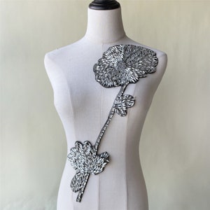 May include: A silver rhinestone flower applique with two blooms and a long stem. The applique is perfect for adding a touch of sparkle to clothing, bags, or home decor.