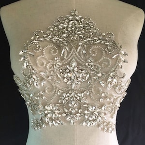 May include: A large, intricate, silver-toned, beaded applique with a floral design. The applique is made of rhinestones and sequins and is perfect for adding a touch of sparkle to any garment.