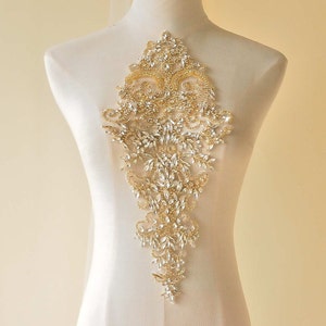 May include: A large, ornate, gold and crystal applique. The applique is shaped like a teardrop and features a delicate floral design. It is perfect for adding a touch of sparkle to any garment.