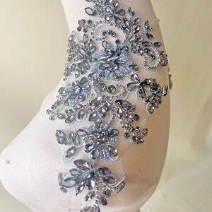 May include: A silver and gray beaded applique with a floral design. The applique is on a white background.
