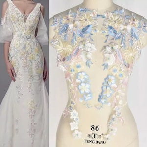 Peut inclure: Une applique en dentelle florale délicate avec des fleurs blanches, bleues et roses. La dentelle est parfaite pour ajouter une touche d'élégance à n'importe quel vêtement.