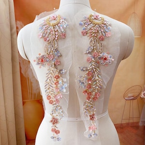 Può includere: Un paio di delicati ricami floreali con decorazioni rosa e dorate. I ricami sono realizzati con paillettes, perline e pizzo, e sono perfetti per aggiungere un tocco di eleganza a qualsiasi capo.