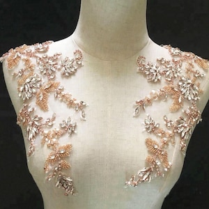 May include: A pair of delicate, floral-shaped embellishments with clear rhinestones and rose gold beads. The embellishments are perfect for adding a touch of sparkle to wedding dresses, bridal accessories, or other special occasion attire.