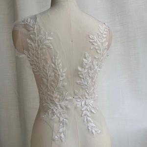 May include: White lace applique featuring a delicate leaf design. The applique is ideal for adding a touch of elegance to any garment.