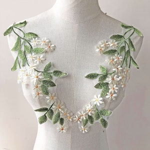 Peut inclure: Applique florale blanche et verte avec de délicates fleurs blanches et des feuilles vertes sur un fond de tissu transparent.