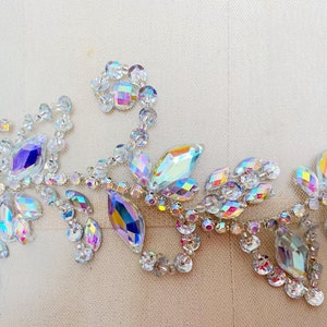 May include: A delicate, iridescent crystal applique featuring a floral design with leaves and small round crystals. The applique is perfect for adding a touch of sparkle to clothing, accessories, or home decor.