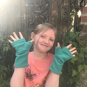 May include: A young person wearing a pink shirt with a butterfly print and teal fingerless gloves. The person is standing in front of a metal gate.