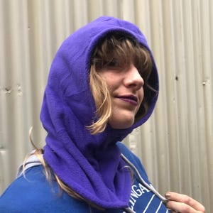 May include: A purple fleece hooded neck warmer with a drawstring. The neck warmer is pulled up over the person's head and covers their neck and ears.