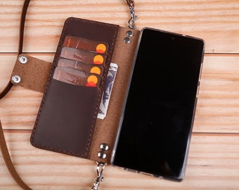 May include: A brown leather phone case with a built-in card holder and a detachable strap. The case is open to reveal a black smartphone.