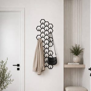 May include: A black metal wall-mounted coat rack featuring a repeating honeycomb hexagonal pattern. The rack includes multiple integrated hooks for hanging items, with a beige jacket and a black shoulder bag currently suspended from the structure.