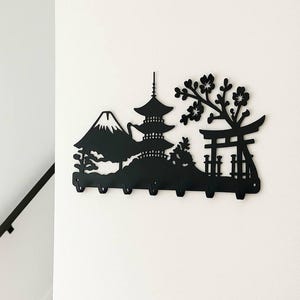 May include: Black metal wall-mounted key holder featuring a Japanese landscape silhouette. The design includes Mount Fuji, a pagoda, a torii gate, and flowering branches. It has six hooks for keys or small items.