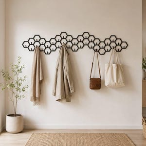 May include: A black wall-mounted coat rack featuring a repeating honeycomb or hexagonal pattern. The metal structure includes multiple integrated hooks for hanging items, with a beige scarf, a tan jacket, a brown bag, and a cream tote bag.