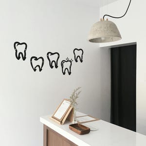 May include: A white countertop with a wooden cabinet underneath. There are five black metal tooth-shaped hooks on the wall above the counter. A concrete pendant light hangs from the ceiling above the counter.