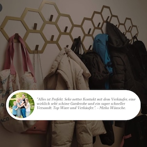 May include: A gold-colored, honeycomb-shaped wall-mounted coat rack with multiple hooks. Various coats, bags, and accessories hang from the hooks. The image includes a customer review with text in German.