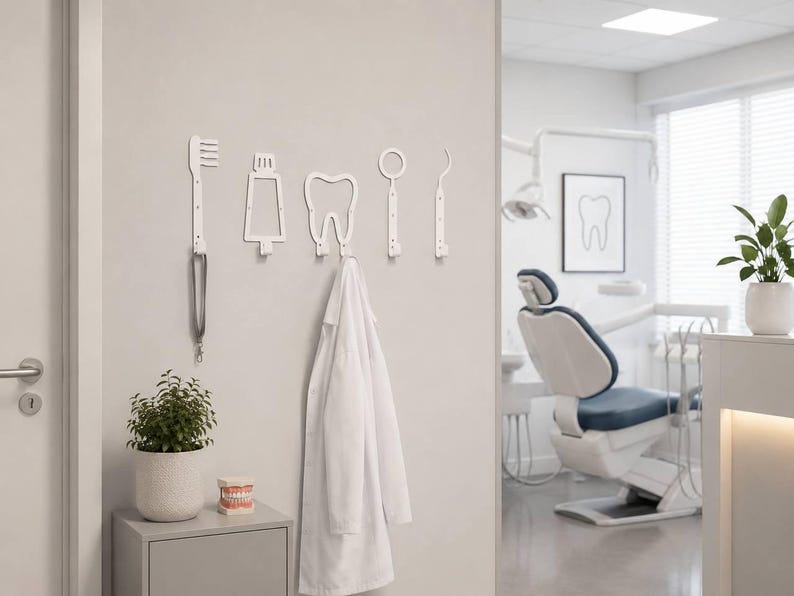 Peut inclure: Un ensemble de cinq pat&egrave;res murales blanches en forme d'instruments dentaires, incluant une brosse &agrave; dents, un tube de dentifrice, une dent, un miroir et une sonde. Une blouse blanche est suspendue &agrave; la pat&egrave;re en forme de dent.