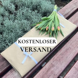 May include: A bouquet of tulips with pink and yellow petals and green leaves, tied with a light blue ribbon, rests on a brown paper-wrapped package. The package is tied with a white ribbon. The text "KOSTENLOSER VERSAND" is visible.