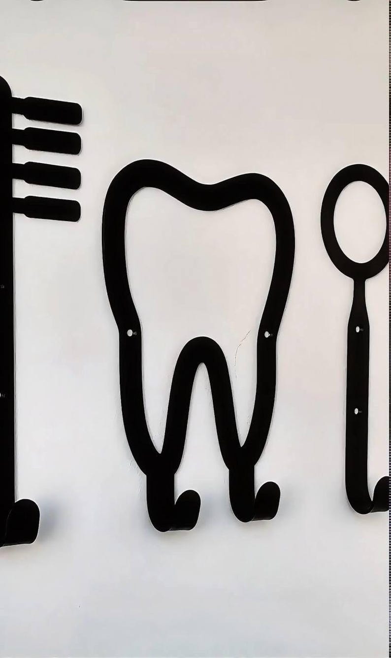Peut inclure: Un ensemble de pat&egrave;res murales en m&eacute;tal noir comprenant un motif central en forme de dent avec deux crochets inf&eacute;rieurs, flanqu&eacute; d'un crochet en forme de brosse &agrave; dents &agrave; gauche et d'un miroir dentaire &agrave; droite, sur fond blanc.