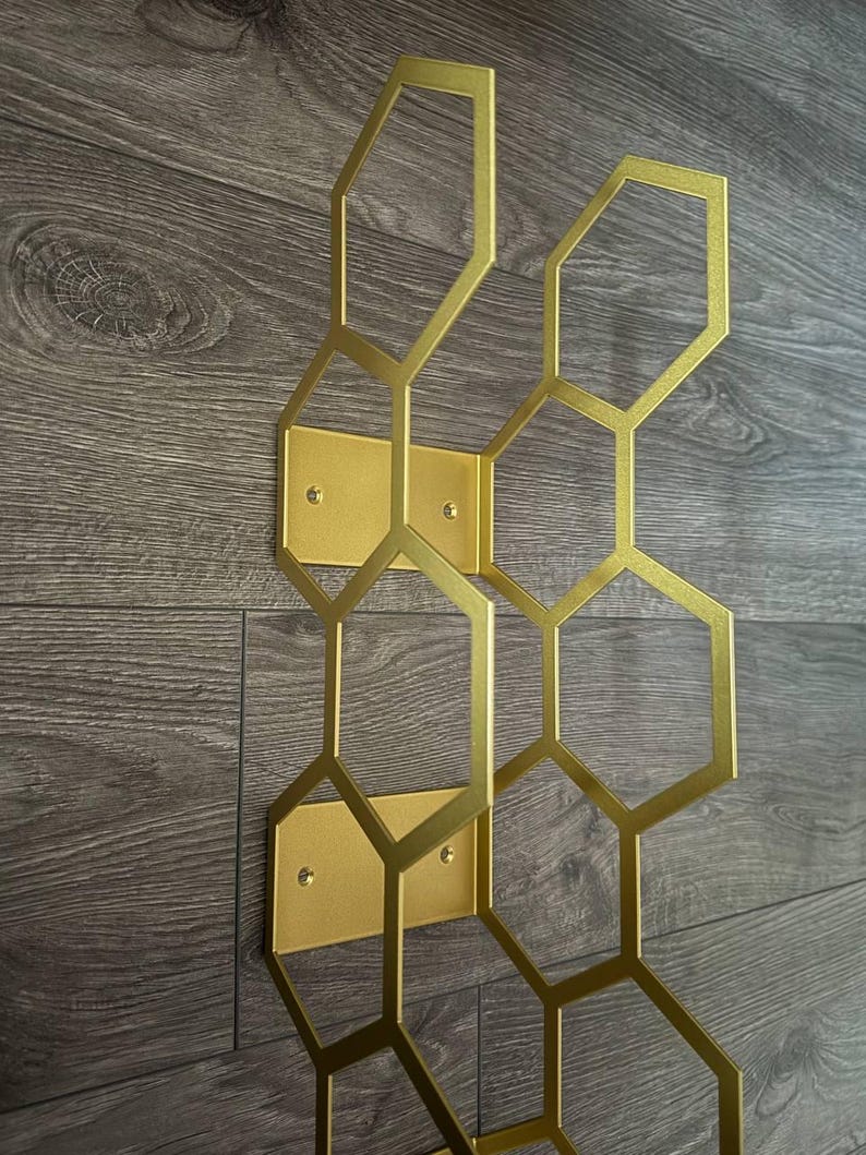 Puede incluir: Decoraci&oacute;n de pared de metal dorado con dise&ntilde;o de panal. El patr&oacute;n geom&eacute;trico est&aacute; compuesto por hex&aacute;gonos interconectados. La decoraci&oacute;n est&aacute; montada sobre placas rectangulares doradas, con orificios para tornillos visibles.