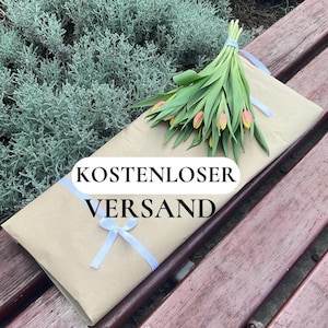 May include: A bouquet of tulips with pink and yellow petals and green leaves, tied with a light blue ribbon, rests on a brown paper-wrapped package. The package is tied with a white ribbon and bow. The text "KOSTENLOSER VERSAND" is visible.