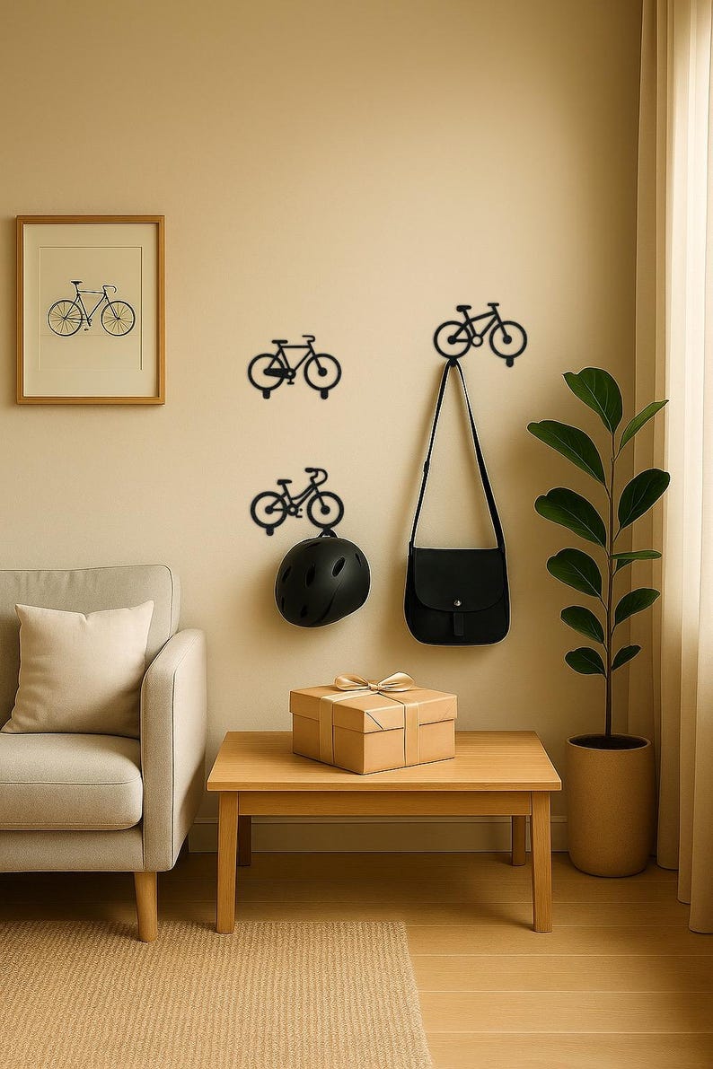 Op de afbeelding: Een kamer met fietsvormige wandhaken, een ingelijste fietsafdruk en een kleine houten tafel. Een zwarte helm en tas hangen aan de haken. Een cadeauverpakking met een gouden lint staat op de tafel. Een plant in een pot staat rechts.