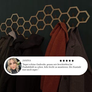 May include: A gold-colored, honeycomb-shaped wall-mounted coat rack with wooden pegs, holding various coats and jackets. The rack is mounted on a dark green wall. A customer review is visible in the image.