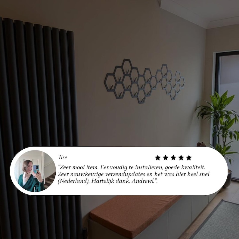 May include: A wall-mounted, honeycomb-shaped coat rack with multiple hooks. The rack is made of a dark gray material and is mounted on a light beige wall. The image also shows a review with text in Dutch.