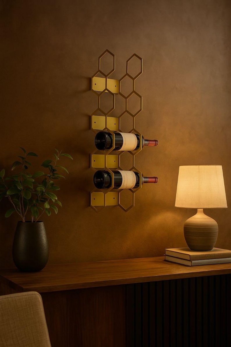Puede incluir: Un botellero de vino montado en la pared con un dise&ntilde;o de panal de abeja dorado, que contiene dos botellas de vino tinto. El botellero est&aacute; fijado a una pared marr&oacute;n. Una l&aacute;mpara y una planta est&aacute;n en el fondo.