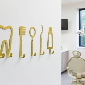 Peut inclure: Un ensemble de cinq pat&egrave;res murales en m&eacute;tal dor&eacute; en forme d'instruments dentaires, comprenant une dent, une brosse &agrave; dents, un miroir dentaire, une sonde et un tube de dentifrice, chacune avec deux petits trous de vis pour la fixation murale.