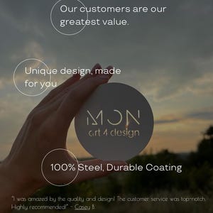 Op de afbeelding: Een rond, lichtgekleurd object met de tekst "MON art 4 clesign" wordt in een hand gehouden. De tekst "100% Steel, Durable Coating" is ook zichtbaar. De achtergrond is een wazige buitensc&egrave;ne met de tekst "Our customers are our greatest value."
