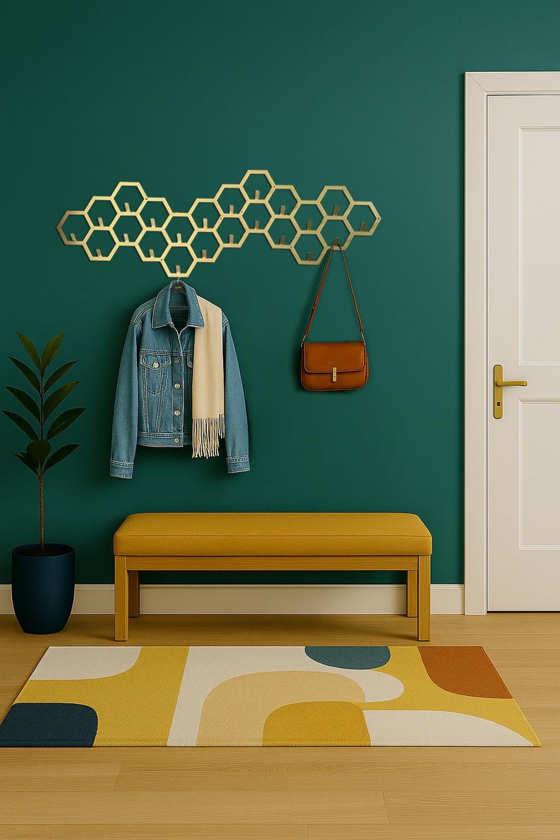 May include: A gold-colored, honeycomb-shaped wall-mounted coat rack with multiple hooks. A denim jacket and scarf hang from the rack, with a brown purse suspended from another hook. A yellow bench and a patterned rug complete the entryway.