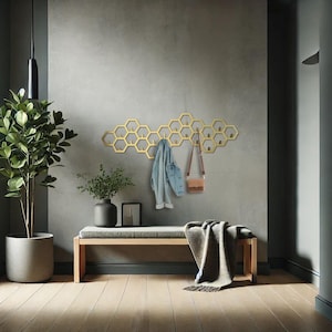 May include: A gold honeycomb-shaped wall mounted coat rack with a blue denim jacket and a brown purse hanging on it. The rack is mounted on a gray wall above a wooden bench with a gray throw blanket.