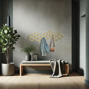 May include: A gold-colored, honeycomb-shaped wall-mounted coat rack with multiple hooks. A denim jacket and a small brown purse hang from the rack. A bench with a gray cushion and a blanket are below the rack. A potted plant is on the left.