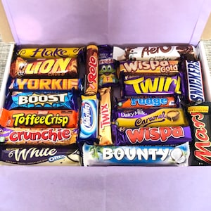 May include: A selection of chocolate bars in a gift box, including brands such as Flake, Lion, and Bounty. The box is lined with lilac tissue paper, and the bars are in their original wrappers.