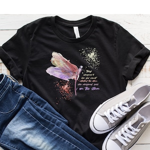 May include: Black t-shirt with a watercolor dragonfly design and the text "They whispered to her you can't withstand the storm she whispered back I am the storm".