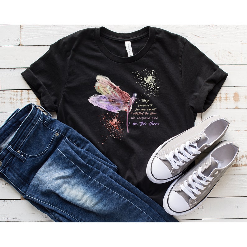 May include: Black t-shirt with a watercolor dragonfly design and the text "They whispered to her you can't withstand the storm she whispered back I am the storm".