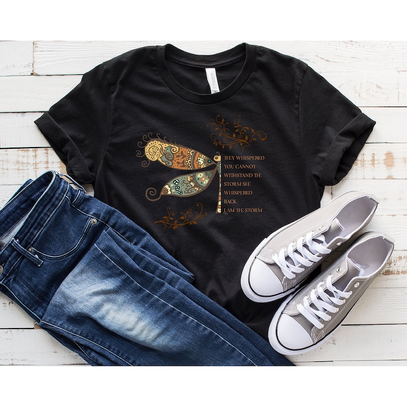 May include: Black t-shirt with a dragonfly graphic and the text "They whispered you cannot withstand the storm. She whispered back I am the storm."