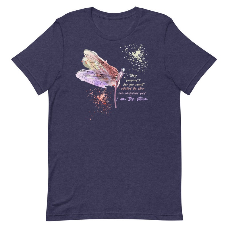 May include: A navy blue t-shirt with a watercolor illustration of a dragonfly and the text "They whispered to her you cannot withstand the storm she whispered back I am the storm".