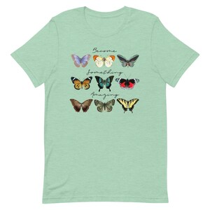 May include: A light green t-shirt with a design of colorful butterflies and the text "Become something amazing".