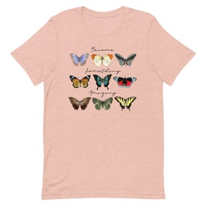 May include: A light pink t-shirt with a graphic of colorful butterflies and the text "Become something amazing".