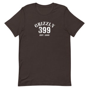 May include: A dark brown t-shirt with a white graphic print that says "Grizzly 399 Est. 1996".