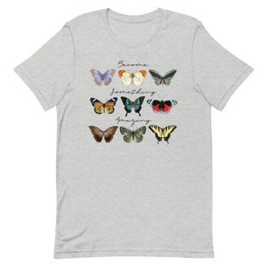 May include: A heather grey t-shirt with a design of colorful butterflies and the text "Become something amazing".
