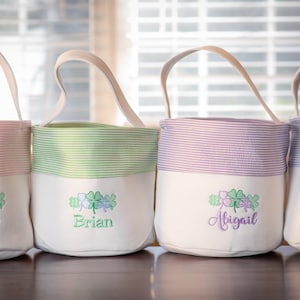 May include: Four personalized canvas Easter baskets with green shamrock embroidery and names "Sofia", "Brian", "Abigail", and "Lucas".