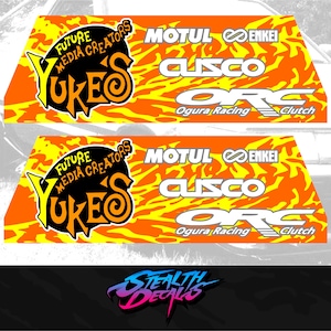 Puede incluir: Dos calcomanías de color naranja y amarillo con un patrón de llamas y texto blanco. La calcomanía superior dice "FUTURE MEDIA CREATORS UKES MOTUL ENKEI CUSCO ORG Ogura Racing Clutch". La calcomanía inferior dice "FUTURE MEDIA CREATORS UKES MOTUL ENKEI CUSCO ORG Ogura Racing Clutch".