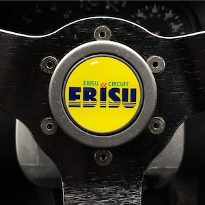 May include: A black steering wheel with a yellow and blue Ebisu Circuit logo in the center.